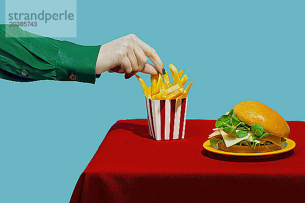 Hand of woman picking up french fries from table against blue background