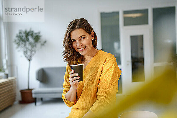 Happy mature woman sitting with coffee cup in living room at home