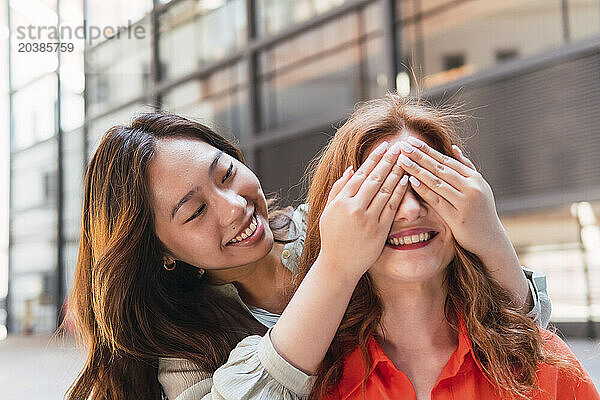 Smiling woman covering eyes of friend with hands