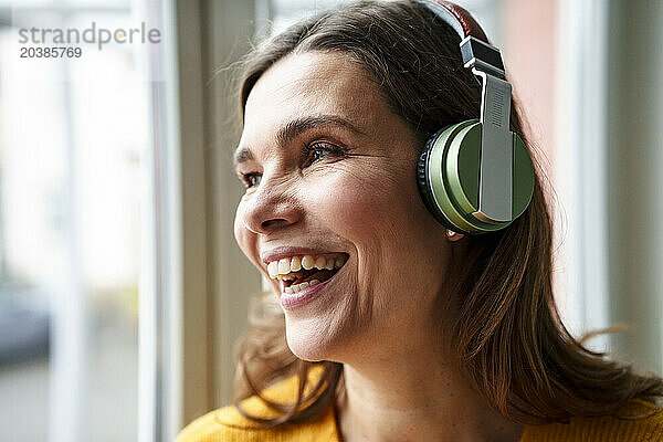 Happy mature woman listening to music through wireless headphones at home