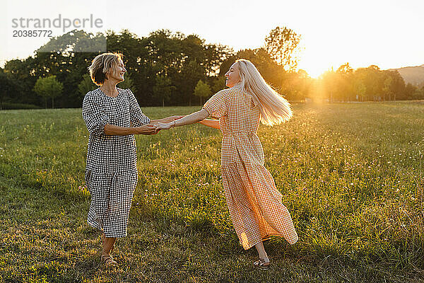 Happy friends holding hands and spinning in park