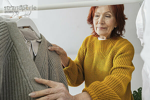 Retired woman choosing sweater from clothes rack at home