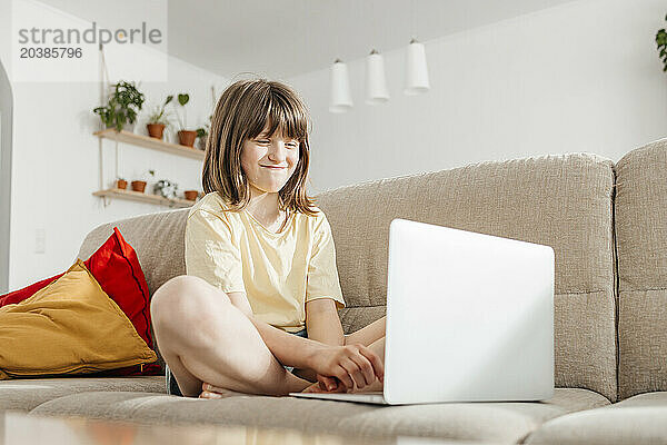 Smiling girl having video call through laptop on sofa at home