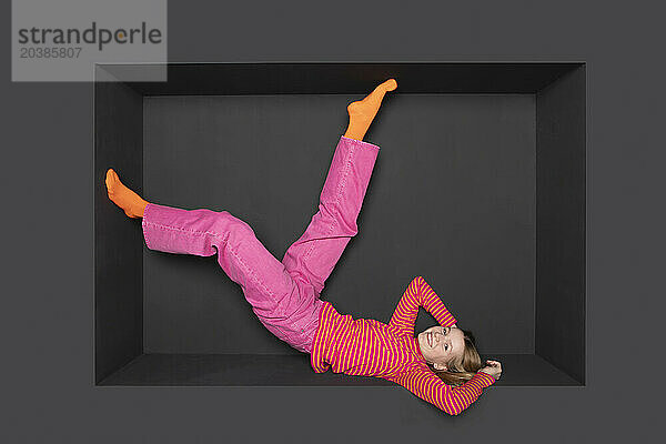 Teenage girl with legs up inside alcove against black background