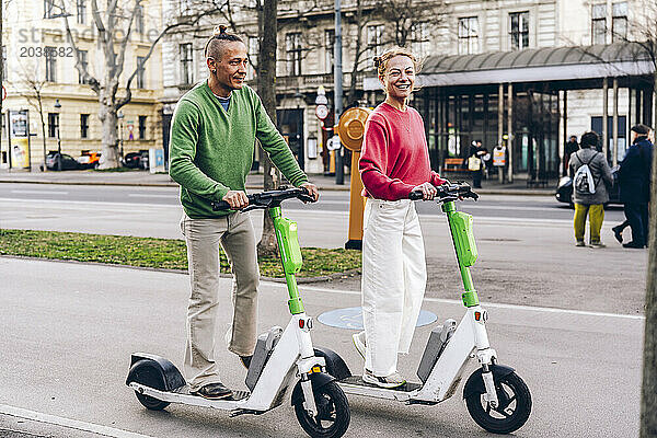 Couple riding electric push scooter on footpath in city