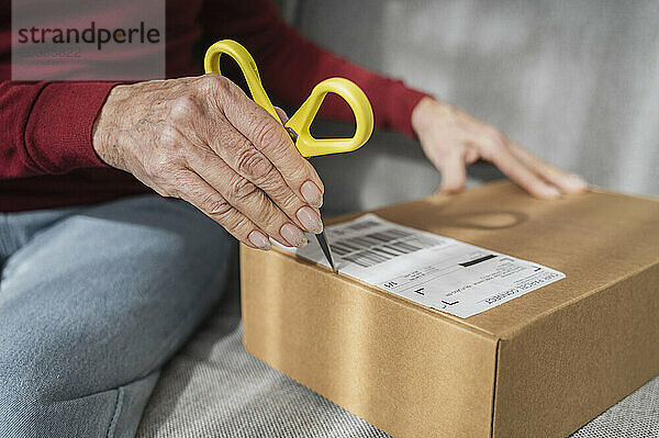 Hand of senior woman opening cardboard box on sofa