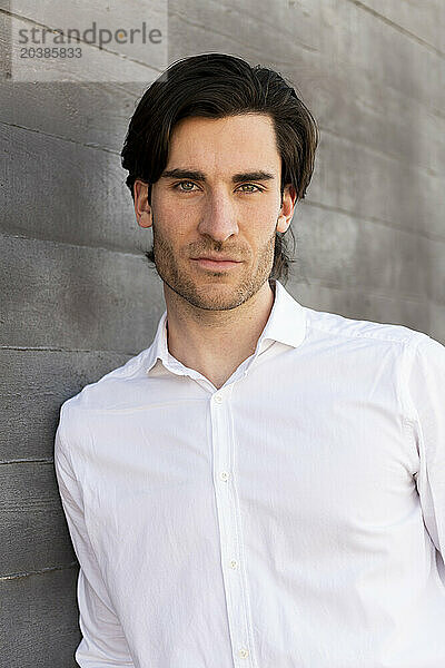 Confident young businessman leaning on wall