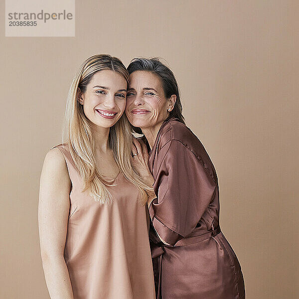 Happy woman standing cheek to cheek with daughter against beige background