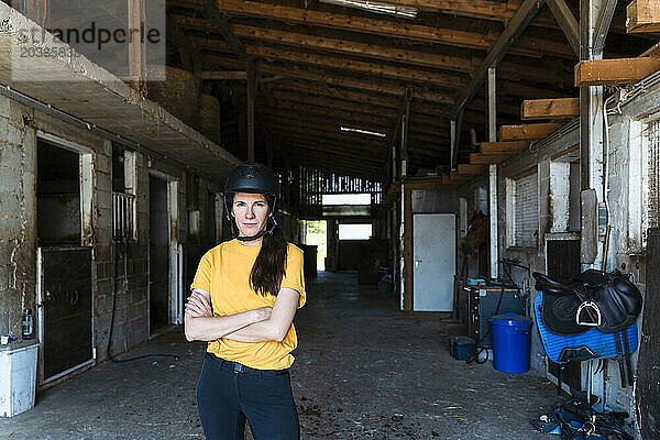 Confidence trainer standing with arms crossed in stable