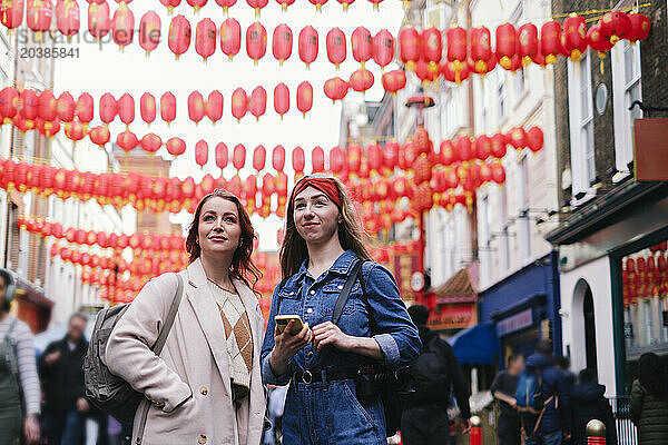 Happy friends standing under hanging Chinese Lanterns in London city