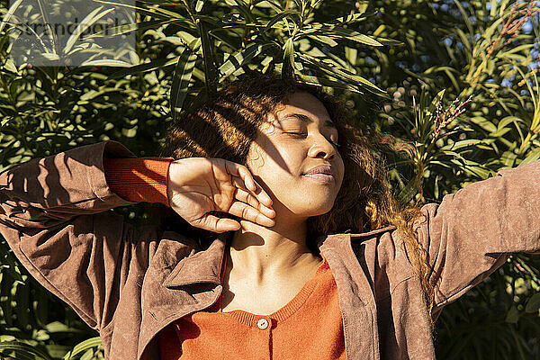 Young woman with eyes closed in front of plants on sunny day