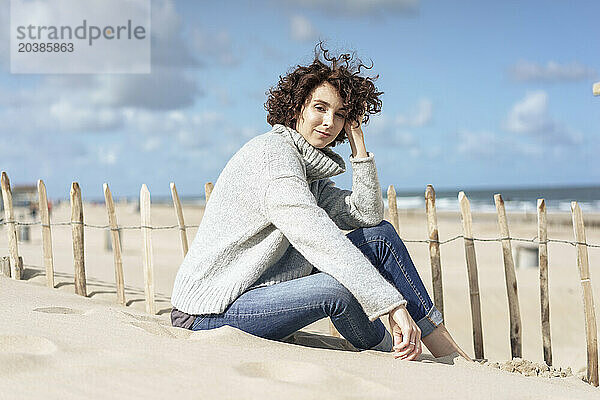 Thoughtful woman sitting on sand at beach