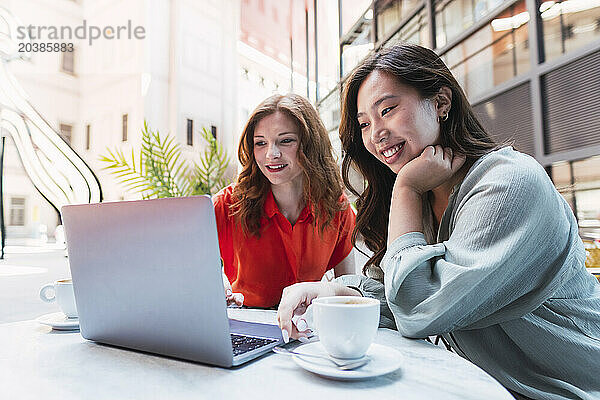 Smiling women using laptop on table sitting at sidewalk cafe
