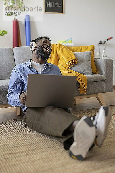 Happy non-binary person wearing wireless headphones and sitting with laptop at home