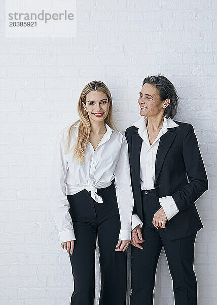 Smiling mother and daughter standing in front of white wall