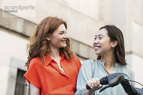 Smiling woman holding handle of electric cycle with friend in city