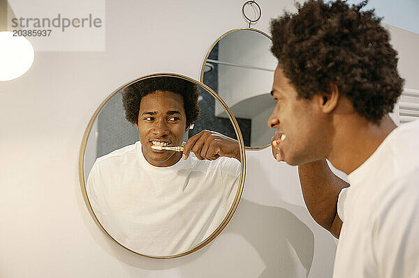 Man brushing teeth looking at mirror reflection in bathroom