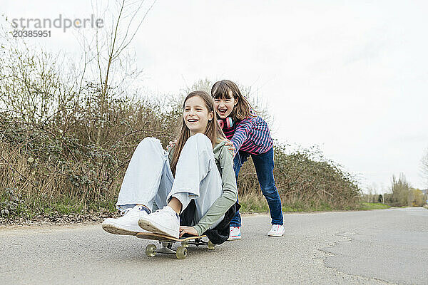 Playful girl pushing friend sitting on skateboard