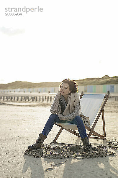 Thoughtful woman sitting on deck chair at beach