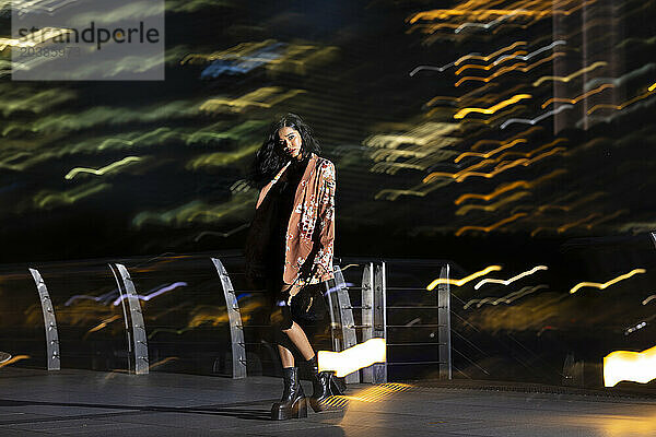 Young woman standing near railing at night