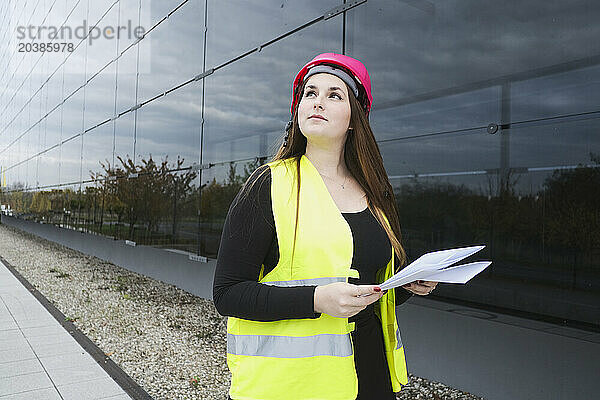 Geodesist wearing hardhat and holding documents near building