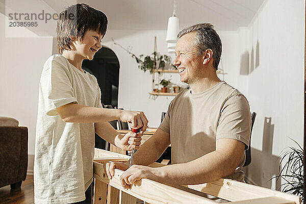 Happy son and father using screwdriver on wooden furniture at home