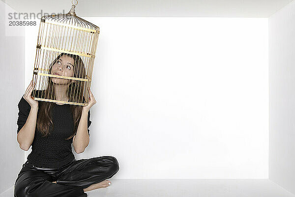 Contemplative teenage girl with birdcage sitting in alcove