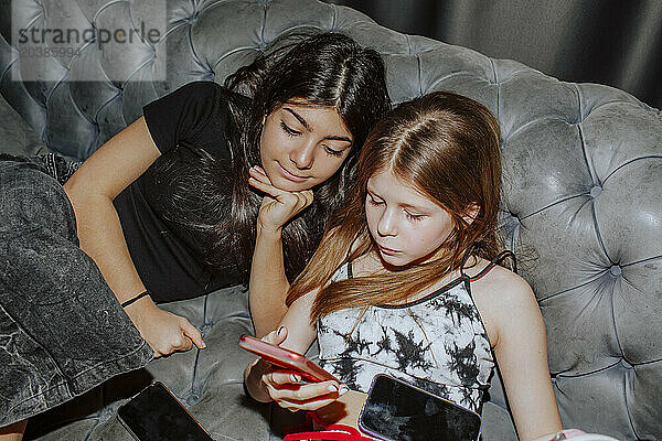 Girl sharing smart phone with friend on sofa at home