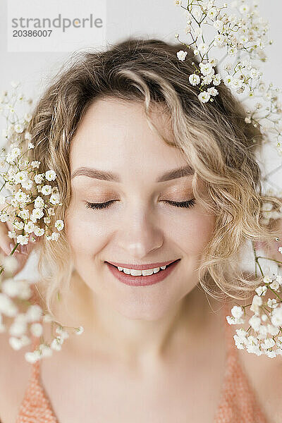 Smiling woman with gypsophila flowers on blond curly hair