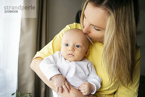 Blond mother kissing son on head at home