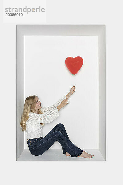 Teenage girl holding heart shape balloon sitting in alcove