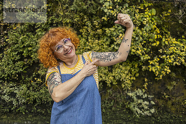 Smiling redhead senior woman flexing muscles with tattoo on it