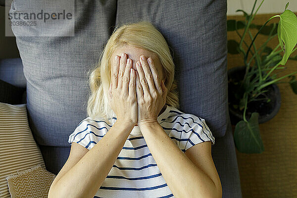 Mature woman covering face with hands at home