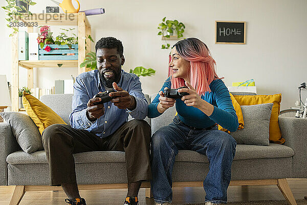 Happy friends playing video game on sofa at home