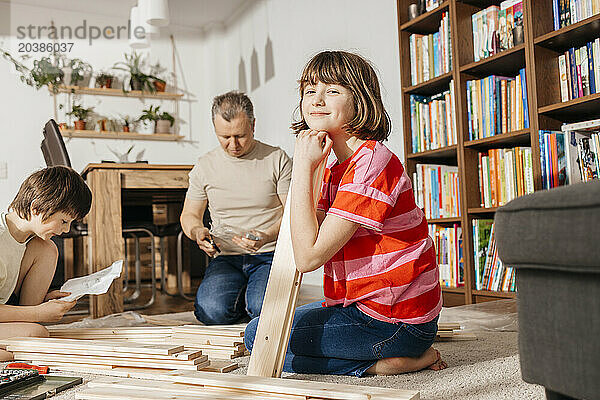 Smiling girl sitting with planks near brother and father in living room