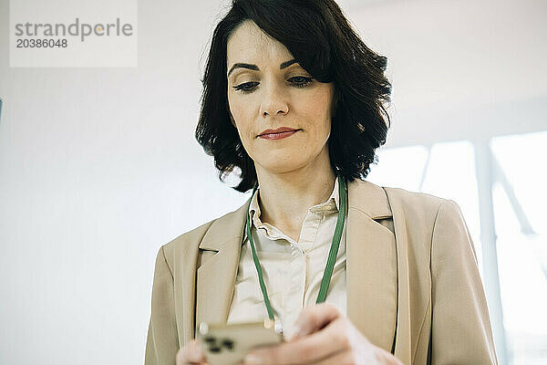 Confident mature businesswoman using smart phone at office