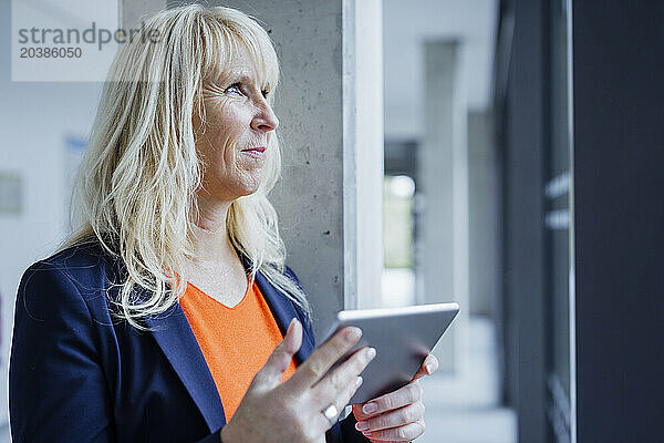 Mature businesswoman with tablet PC in office corridor