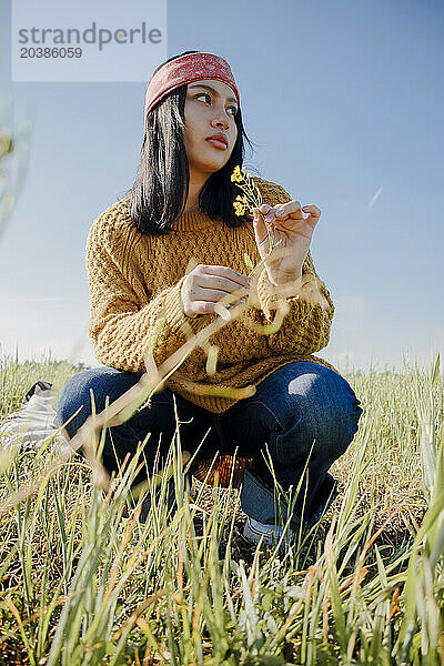 Young woman holding flower and crouching in field