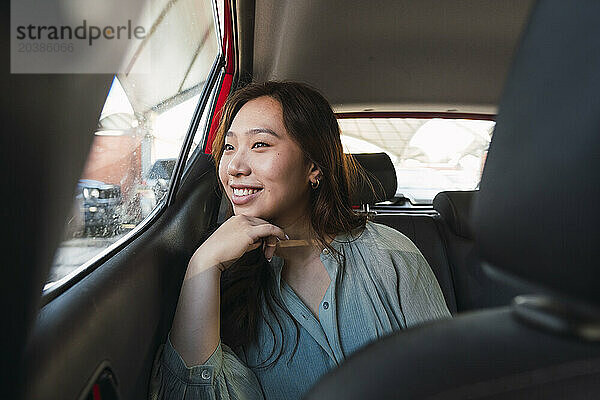 Smiling woman with hand on chin looking through car window