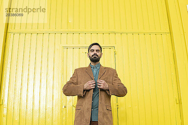 Man wearing brown jacket and standing in front of yellow wall