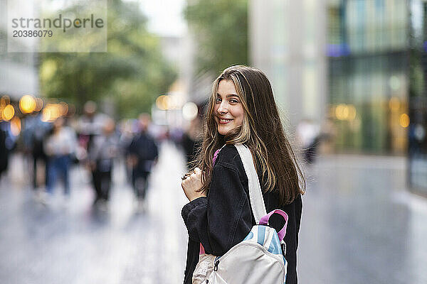 Happy young woman with backpack in city