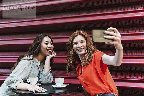 Happy woman taking selfie with friend through smart phone near shutter