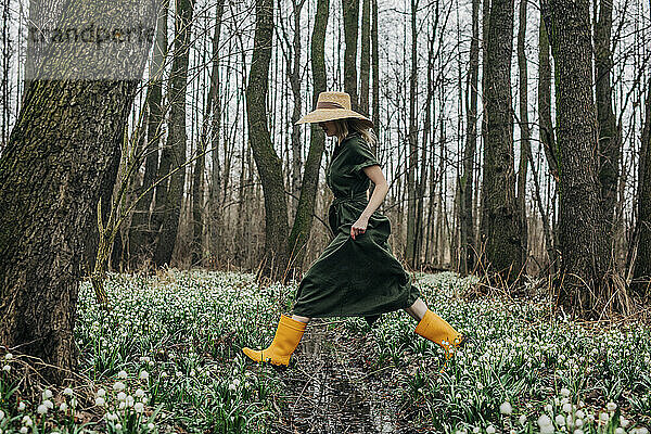 Woman crossing over creek amidst Lily-of-the-valley flowers in forest