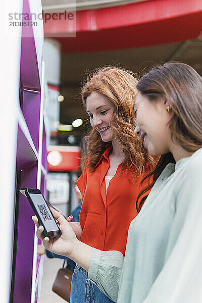 Smiling friends using smart phones near ticket vending machine