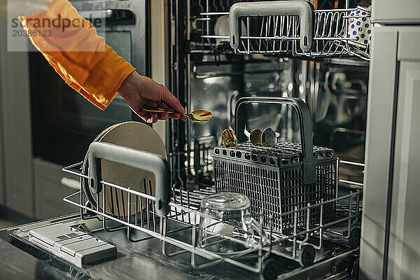 Hand of woman picking up spoon from dishwasher at home