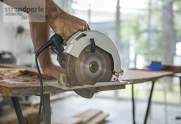 Carpenter cutting timber with electric circular saw at workshop