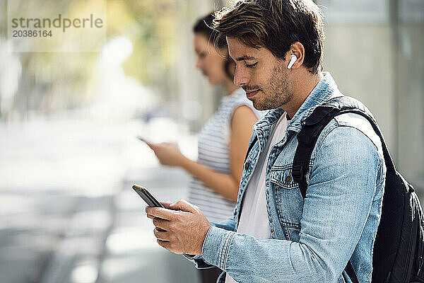 Man using smart phone with girlfriend in background