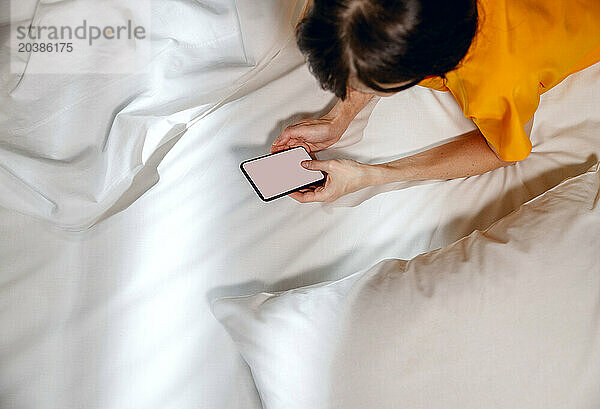 Woman lying with smart phone on bed at home