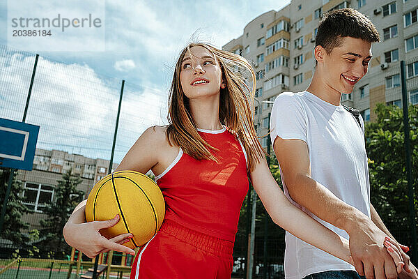 Smiling teenage friends holding hands and walking in school yard