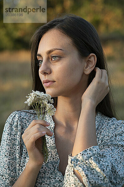 Beautiful young woman holding wildflower near face